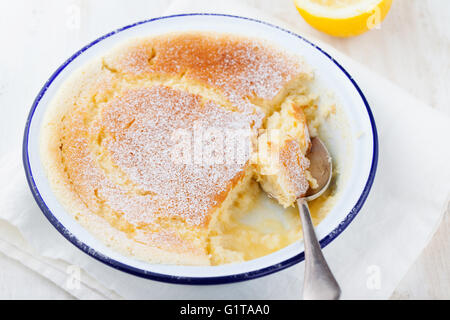 Zitrone-Pudding-Kuchen mit frischen Zitronen auf einem weißen Hintergrund aus Holz. Stockfoto