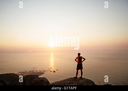 Männliche Läufer auf Felsen, Blick auf den Sonnenuntergang mit Meerblick Stockfoto