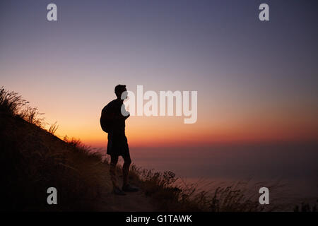 Silhouette des männlichen Wanderer unterwegs mit Blick auf Meer bei Sonnenuntergang Stockfoto