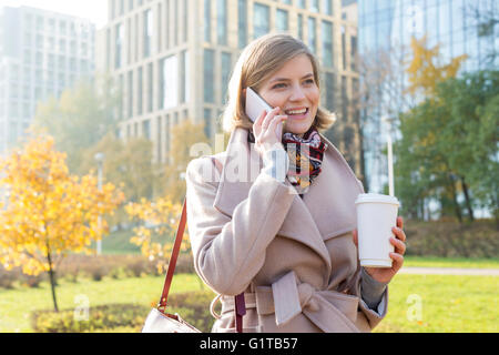 Lächelnd Geschäftsfrau mit Kaffee reden über Handy im Stadtpark Stockfoto