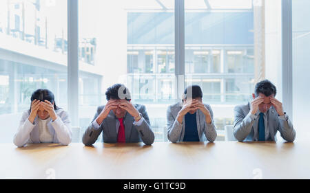 Betonte Geschäftsleute mit Kopf in Händen am Konferenztisch Stockfoto