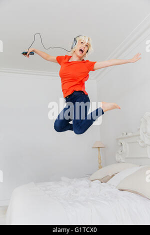 Verspielte Frau springen auf Bett Musikhören mit Kopfhörer und MP3-player Stockfoto