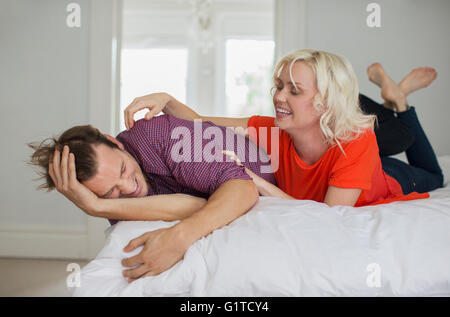 Verspielte Frau kitzeln Mann auf Bett Stockfoto