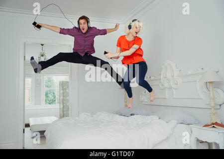Verspieltes paar springen auf Bett und Musikhören mit MP3-Player und Kopfhörer Stockfoto