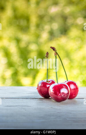 Drei Kirschen mit Stielen auf hölzernen Hintergrund. Viele Textfreiraum Stockfoto