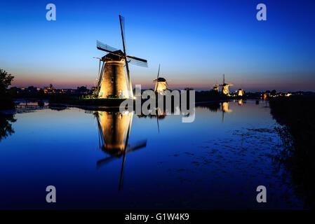 Historischen beleuchteten Windmühlen in Kinderdijk mit Spiegelbild im Wasser des Kanals unter einem blauen Stunde Himmel in den Niederlanden. Stockfoto