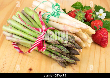 Grüner Spargel mit frischen Erdbeeren auf hellem Holz. Veganes Essen, vegetarische und gesunde Koch-Konzept. Stockfoto