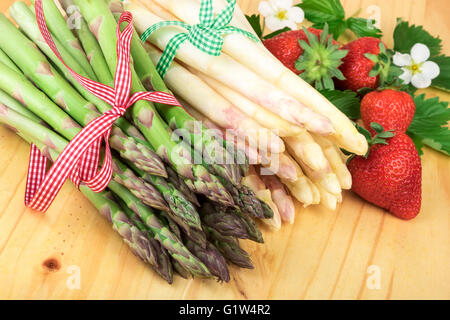 Grüner Spargel mit frischen Erdbeeren auf hellem Holz. Gesund kochen-Konzept. Stockfoto