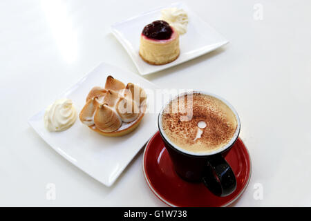 Zitronen-Baiser und Erdbeer Käsekuchen mit einer Tasse Kaffee auf weißen Tisch Stockfoto