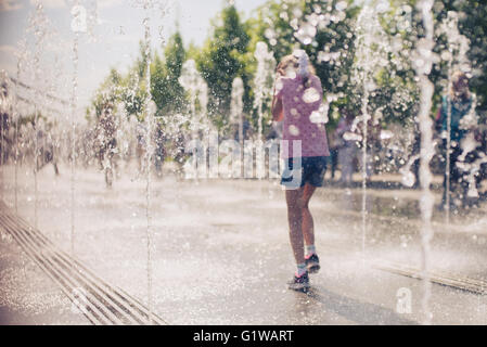 Kleine süße Mädchen in offenen Straße Brunnen an heißen sonnigen Tag zu Fuß. Hinten Sie Ansicht von. Stockfoto