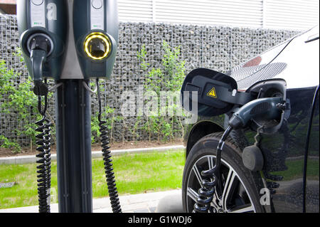 Ein Elektroauto wird auf einem Parkplatz geparkt und ist an ein Kraftwerk aufgeladen wird. Stockfoto