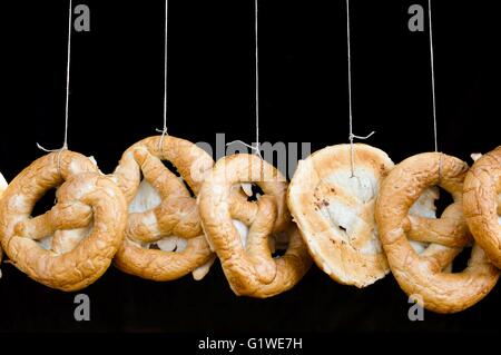 Frisch gebackene hausgemachte deutsche Brezeln hängen auf dem Markt mit schwarzem Hintergrund Stockfoto