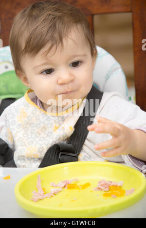 Porträt von niedlichen einjähriges Baby mit schmutziges Hemd Essen mit den Händen Stockfoto