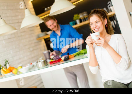 Frau trinkt Kaffee, während ein Mann eine Mahlzeit bereitet Stockfoto