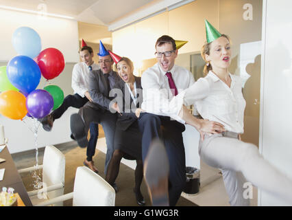 Spielerische Geschäftsleute mit Partyhüte tanzen in Conga Linie Stockfoto