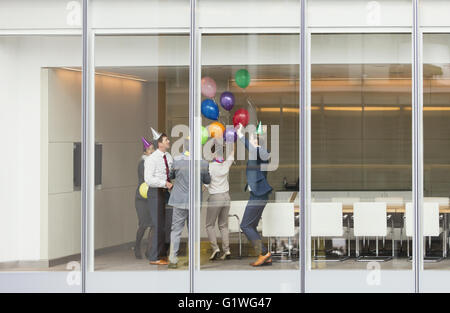 Spielerische Geschäftsleute in Partyhüte feiern mit Luftballons im Konferenzraum Stockfoto