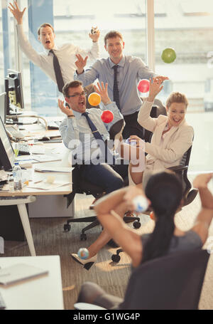 Spielerische Geschäftsleute bunten Plastikbällen bewerfen einander im Büro Stockfoto