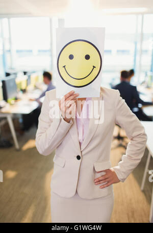 Porträt der Geschäftsfrau hält Smiley Gesicht Ausdruck über ihr Gesicht im Büro Stockfoto