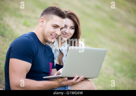 Porträt von positiven jungen Mann und lächelnde schöne Frau in Freizeitkleidung auf Sommertag auf dem Rasen im Park sitzend Stockfoto