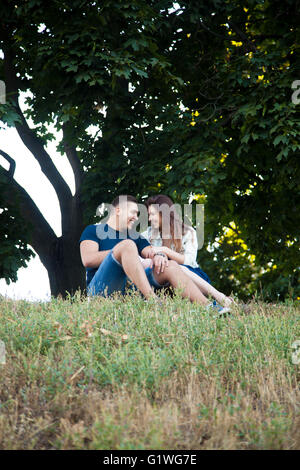 Schöne glückliches junges Paar in Liebe tragen legere Kleidung unter Ahornbaum im Park entspannen, sitzen zusammen auf Rasen Stockfoto