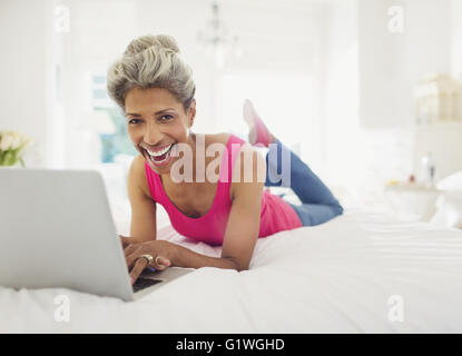 Porträt lachende Reife Frau mit Laptop am Bett Stockfoto
