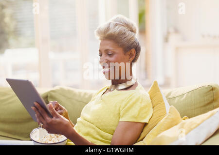 Reife Frauen mit digital-Tablette Essen Popcorn auf sofa Stockfoto
