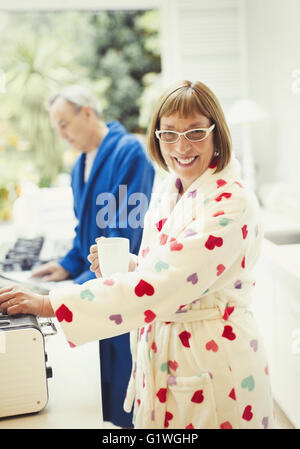 Porträt lächelnd Reife Frau im Bademantel am Küchentisch Kaffee trinken Stockfoto
