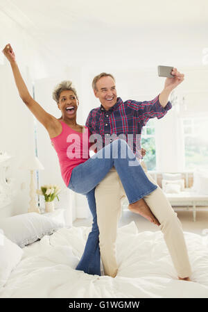Spielerische älteres paar nehmen Selfie stehend auf Bett Stockfoto