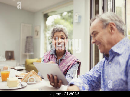 Älteres paar lachend und mit digital-Tablette am Frühstückstisch Stockfoto