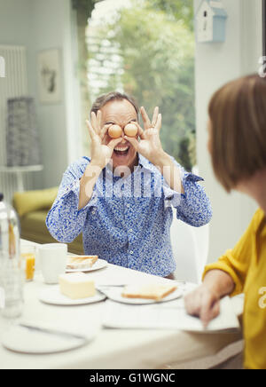 Spielerische Reife Manndeckung Augen mit Eiern am Frühstückstisch Stockfoto