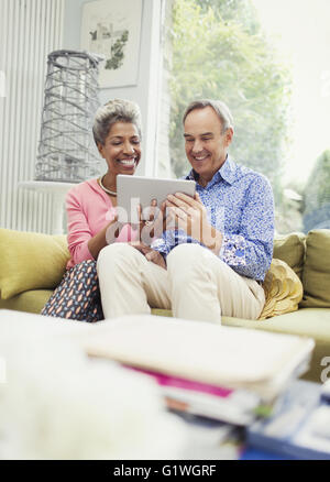 Lächelnd älteres Paar teilen digital-Tablette auf Sofa im Wohnzimmer Stockfoto