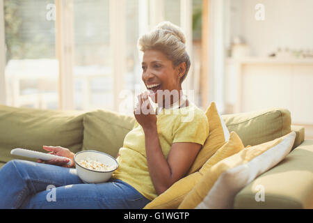 Reife Frau Essen Popcorn und Fernsehen auf dem Sofa im Wohnzimmer Stockfoto