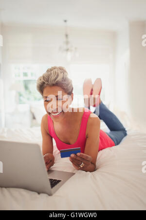 Reife Frau mit Kreditkarte online-shopping mit Laptop am Bett Stockfoto