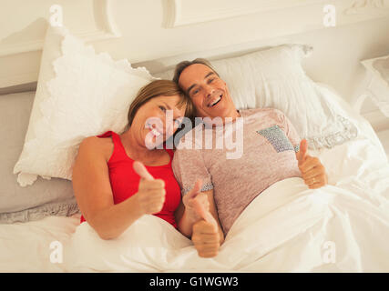 Porträt verspielt älteres paar gestikulieren Daumen im Bett Stockfoto