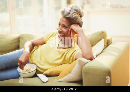 Komfortable Reife Frau vor dem Fernseher und Essen Popcorn auf Sofa im Wohnzimmer Stockfoto