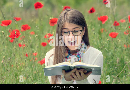 Teenager-Mädchen lesen Sie ein Buch im Mohnfeld Stockfoto