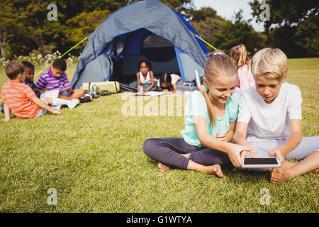 Lächelnde Kinder suchen ihr Tablet mit anderen Kindern dahinter Stockfoto