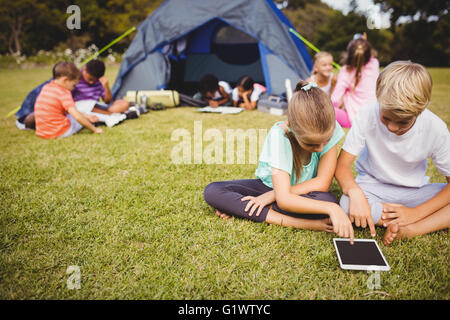 Lächelnde Kinder suchen ihr Tablet mit anderen Kindern dahinter Stockfoto