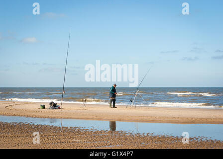 Ein Fischer-Mann mit zwei Angelruten am Nordseestrand im Meer-Angelwettbewerb in Egmond-Aan-Zee Niederlande Stockfoto