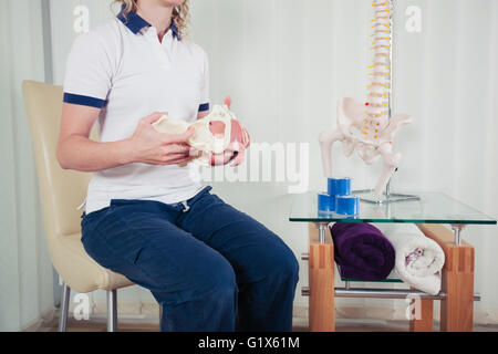 Physiotherapeut / in ihrem Büro sitzt und hält ein Modell des menschlichen Beckens Stockfoto