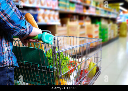 Mann schieben Einkaufswagen voller Lebensmittel im Supermarkt Gang. Erhöhte Sicht nach hinten. horizontale Komposition Stockfoto