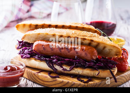 Grillwurst-Sandwich mit süßen Rotkohl Krautsalat, Senf und Tomatensauce auf Holzbrett Stockfoto