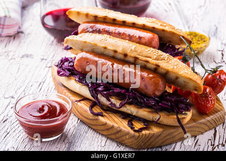 Grillwurst-Sandwich mit süßen Rotkohl Krautsalat, Senf und Tomatensauce auf Holzbrett Stockfoto