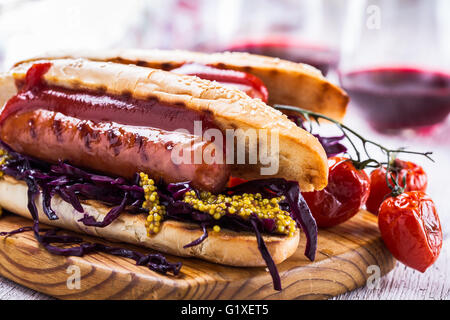 Grillwurst-Sandwich mit süßen Rotkohl Krautsalat, Senf und Tomatensauce auf Holzbrett Stockfoto