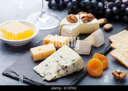 Auswahl an Käse mit Honig, Nüssen und Trauben auf einem modernen Cutting Board Schiefer Hintergrund. Stockfoto
