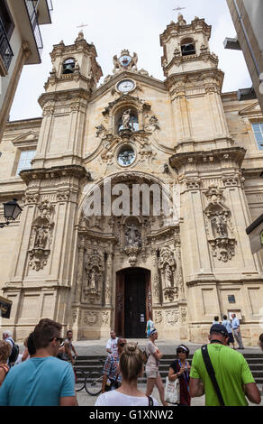 Vorderansicht der Basilika/Iglesia de Santa Maria del Coro, San Sebastian, Spanien mit den kunstvoll verzierten religiösen Schnitzereien und Touristen im Vordergrund Stockfoto