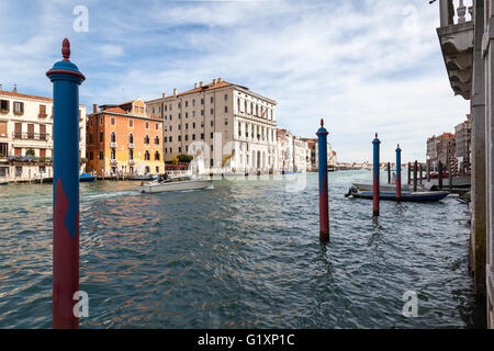 Sonnendurchflutete Gebäude am Canale Grande in Venedig Eine Reihe von blauen und roten Anlegestellen und ein kanal Start vorbei an einem blauen Himmel Stockfoto