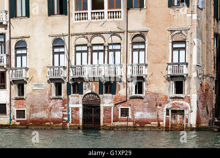 Sonnendurchflutete zerbröckelnde Gebäude mit einem Wassertor auf Kanalhöhe und weißen Balkons am Canale Grande in Venedig, Italien Stockfoto