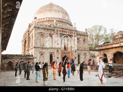 Junge Männer und Frauen praktizieren Yoga am frühen Morgen am Bara-Gumbad Grab. Stockfoto