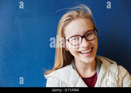 Lächelnde blonde Frau steht vor einer blauen Wand Stockfoto